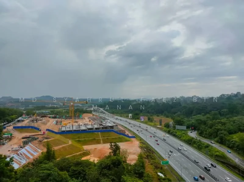 Exterior features: construction site with cranes, earthworks in progress, blue construction hoarding, highway visible in foreground, surrounding greenery, cloudy sky.