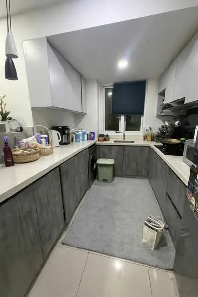 Kitchen features: grey cabinetry, white countertop, stainless-steel sink, chrome faucet, built-in stove, microwave, kettle, toaster, basket for storage, grey area rug, tile flooring, window with blue roller blinds, wall-mounted cabinets; style: modern.