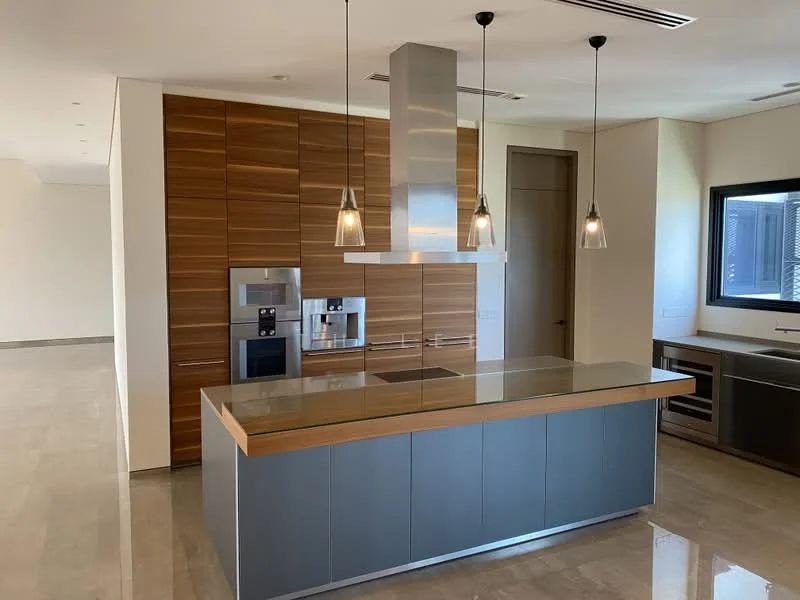 Kitchen features: island kitchen with countertop, stainless-steel range hood, built-in oven, built-in coffee machine, stainless-steel fridge, wood cabinetry with horizontal grain, marble flooring, pendant lighting, recessed ceiling lights, large window, grey cabinetry, open layout; style: modern.