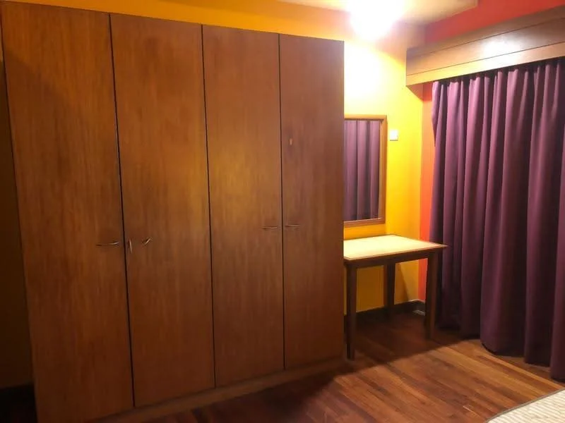 Bedroom features: wooden flooring, orange painted walls, purple curtains, built-in wooden wardrobe with multiple doors, wooden desk, ceiling light fixture.