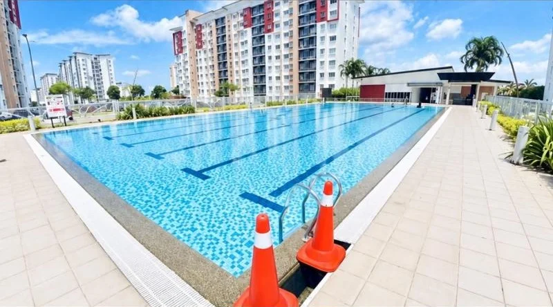 Exterior type: swimming pool deck; features: infinity pool, pool deck with tiled paving, glass safety railing, surrounding high-rise condominium towers, white and red facade towers, palm trees, landscaped planting beds, poolside clubhouse building, clear blue sky, lane markings in pool, stainless-steel pool ladder; style: modern.