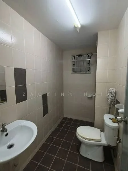 Bathroom features: white ceramic sink, chrome faucet, white toilet, grey tiled flooring, light beige wall tiles, dark beige accent tiles, window with metal grille, overhead fluorescent lighting.