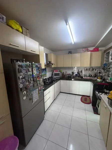 Kitchen features: light wood cabinetry, black countertop, stainless-steel fridge, built-in oven, 4-burner gas hob, double-bowl stainless-steel sink, chrome pull-down faucet, white tiled backsplash, white tiled flooring, recessed ceiling lights, open shelving, decorative magnets on fridge, kitchen rug in pink, microwave, kettle; style: modern.