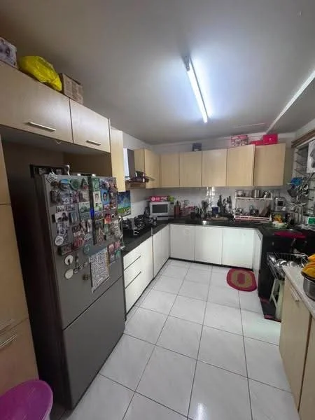 Kitchen features: light wood cabinetry, black countertop, stainless-steel fridge, built-in oven, freestanding range oven, microwave, double-bowl stainless-steel sink, chrome pull-down faucet, white tiled flooring, LED strip lighting, wall-mounted shelves, decorative magnets on fridge, kitchen utensils, black backsplash, area rug in pink; style: modern.