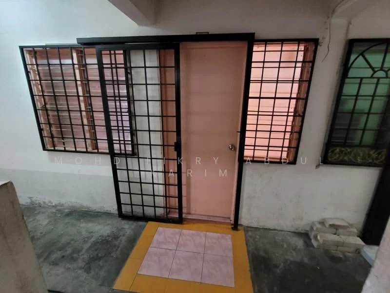 Room features: metal security grille door, single door, two windows with metal grilles, pink door, grey concrete flooring, yellow and pink tiled flooring, white walls, window treatments with decorative patterns.