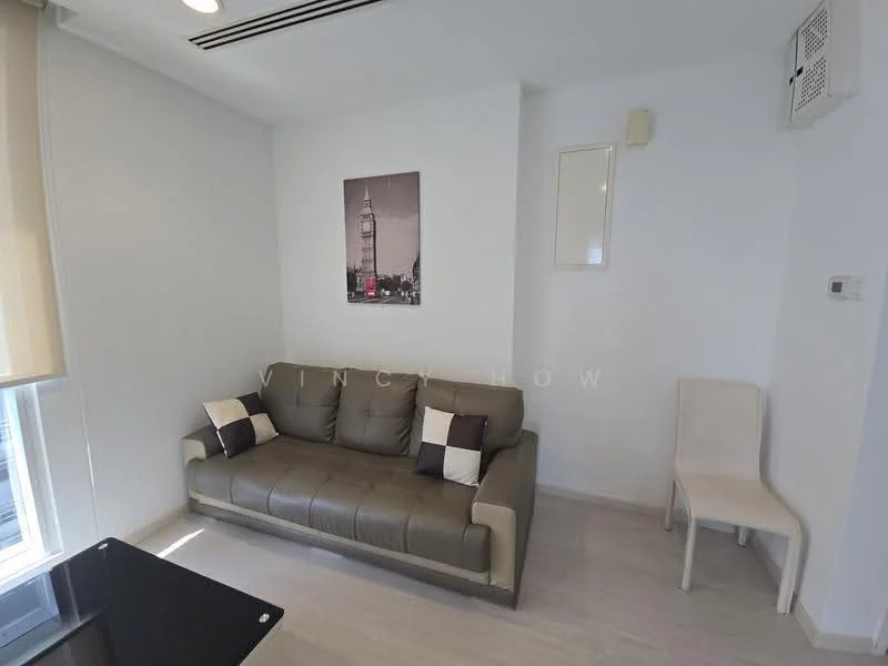 Living features: grey leather sofa, decorative cushions in black and white, light wood flooring, white painted walls, wall-mounted air conditioning unit, framed artwork on wall, single white chair, window with sheer curtains, recessed ceiling lights; style: modern.