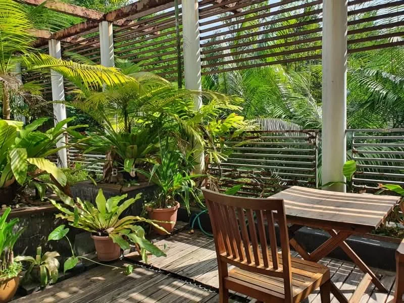 Room features: wooden deck flooring, wooden dining table, wooden chairs, potted plants, tropical greenery, lattice overhead structure, railings, sunlight filtering through leaves; style: tropical; view: garden.