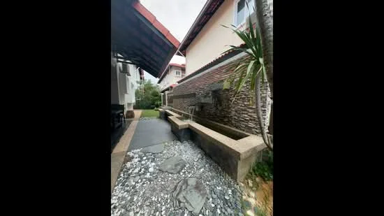 Exterior type: detached bungalow; features: stone cladding on wall, water feature with flowing water, landscaped garden area, pebble pathway, overhanging roof, potted plants, concrete bench, sliding glass door, manicured lawn; style: modern.
