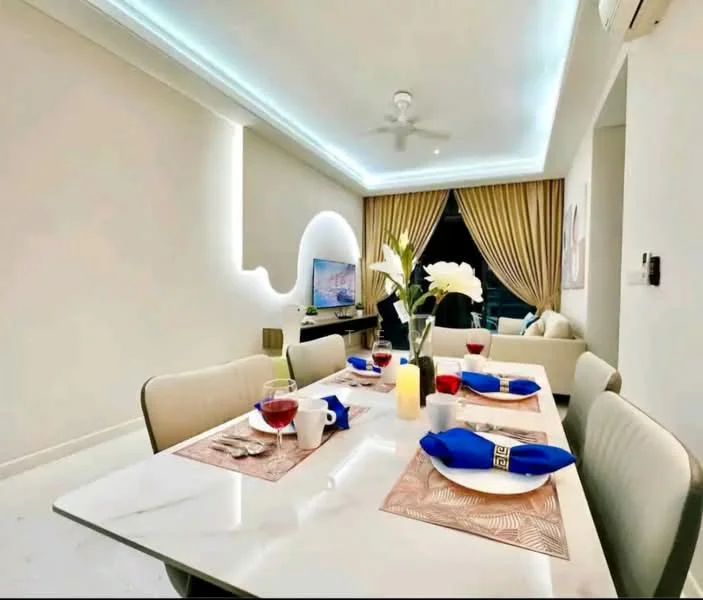 Dining features: white marble dining table, 4 upholstered dining chairs, blue table napkins, decorative placemats, red wine glasses, white flower vase, LED strip lighting on ceiling, wall-mounted TV, cream curtains, sofa in background, light-colored walls, ceiling fan; style: modern.