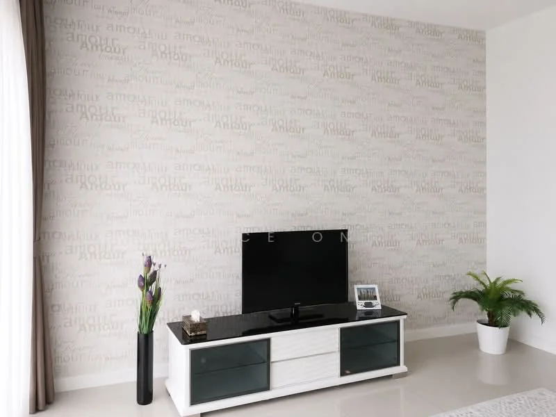 Living features: cream wallpaper with text pattern, white painted walls, glossy beige tile flooring, black TV console with glass doors, wall-mounted flat-screen TV, decorative plant in white pot, tall vase with purple flowers, sheer curtains, natural light from window; style: modern.