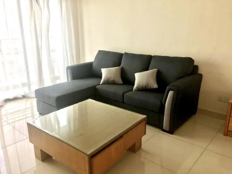 Living features: L-shape sectional sofa in dark grey, 2 decorative cushions in light grey, glass coffee table with wooden base, cream painted walls, large windows with sheer curtains, glossy ceramic tile flooring, natural light from windows; style: modern.