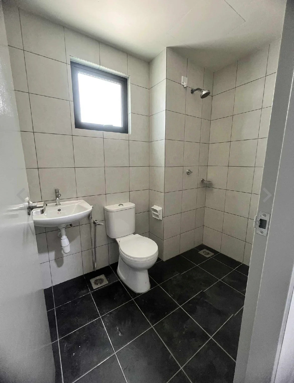 Bathroom features: white tiled walls, grey tiled flooring, window with black frame, single-sink vanity with wall-mounted faucet, one-piece toilet, handheld shower, shower wall with tiles, chrome showerhead; style: modern.
