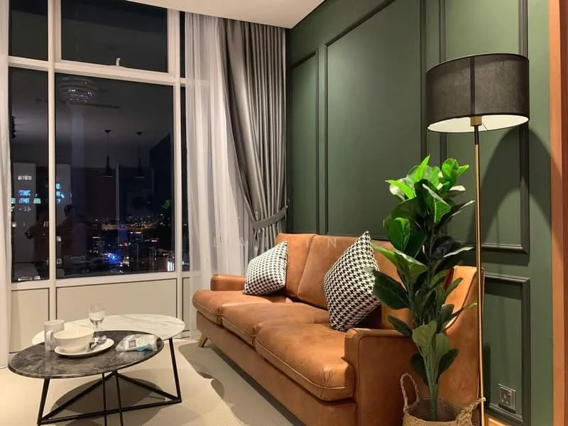 Living features: brown leather sofa, black and white patterned throw pillows, round marble coffee table, glass of water on table, decorative plant in pot, floor lamp with black shade, green accent wall with paneling, floor-to-ceiling windows with sheer curtains, city skyline view at night; style: modern; view: city.