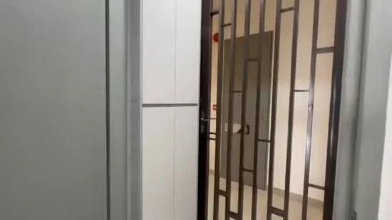 Room features: metal gate with geometric pattern, white cabinetry, light grey walls, neutral tile flooring, door with handle, light switch, wall-mounted fire alarm, door frame; style: modern.
