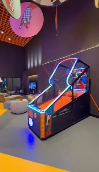 Room features: arcade basketball game, neon lighting, black walls, wooden ceiling with grid pattern, multicolored flooring, sofa seating, television, decorative wall art; style: modern.
