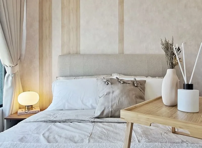 Bedroom features: queen-size bed, upholstered headboard, white bedding, decorative throw pillow, wooden bedside table, table lamp with round shade, decorative vase, dried flowers, light-colored wall with vertical wood paneling, curtains, wooden tray; style: modern.