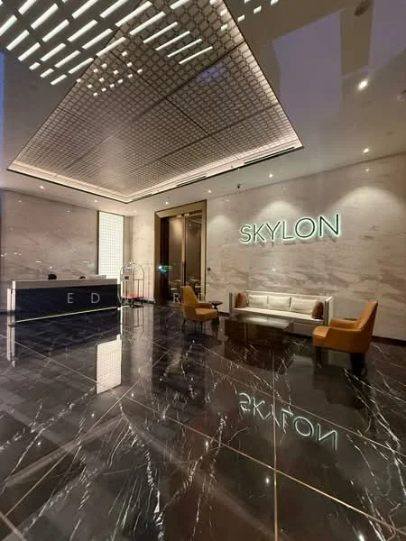 Lobby features: marble flooring with black and white veining, reception desk with backlit signage, sofa in cream upholstery, two accent chairs in mustard yellow, modern ceiling with geometric light fixtures, wall-mounted lighting, large glass entrance doors, decorative wall panels, elegant decor elements; style: modern.