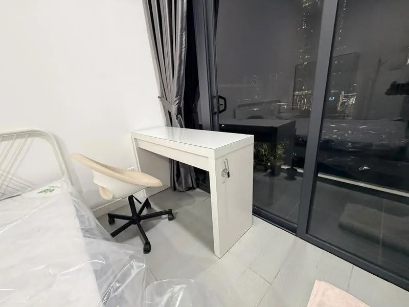 Room features: white desk, rolling office chair, floor-to-ceiling windows, grey curtains, wooden flooring, city view, bed with mattress, decorative plants; style: modern; view: city.