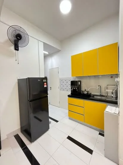 Kitchen features: yellow upper cabinets, black lower cabinets, black countertop, white tiled backsplash, stainless-steel sink, chrome faucet, black refrigerator, built-in coffee machine, white trash bin, ceiling fan, white walls, black and white tiled flooring, door to hallway; style: modern.