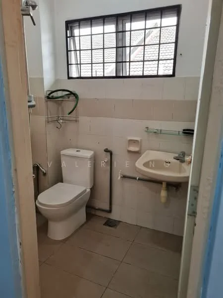 Bathroom features: white tiled walls, cream tiled flooring, one-piece toilet, sink with wall-mounted faucet, mirror above sink, shower head mounted on wall, window with metal grille, towel rack, plumbing pipe visible.