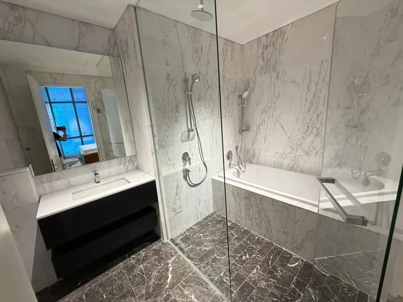Bathroom features: marble tile walls, glass shower enclosure, bathtub with glass panel, double shower heads, single-sink vanity with black cabinet, mirror above vanity, chrome faucets, dark stone flooring, recessed lighting, rain shower head; style: modern.