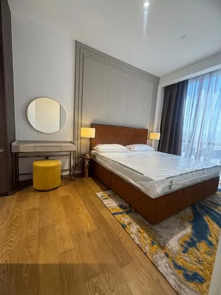 Bedroom features: king-size bed, upholstered headboard, two bedside lamps, round mirror, wooden flooring, area rug with abstract pattern, yellow ottoman, built-in wardrobe, floor-to-ceiling windows with curtains; style: modern; view: city.