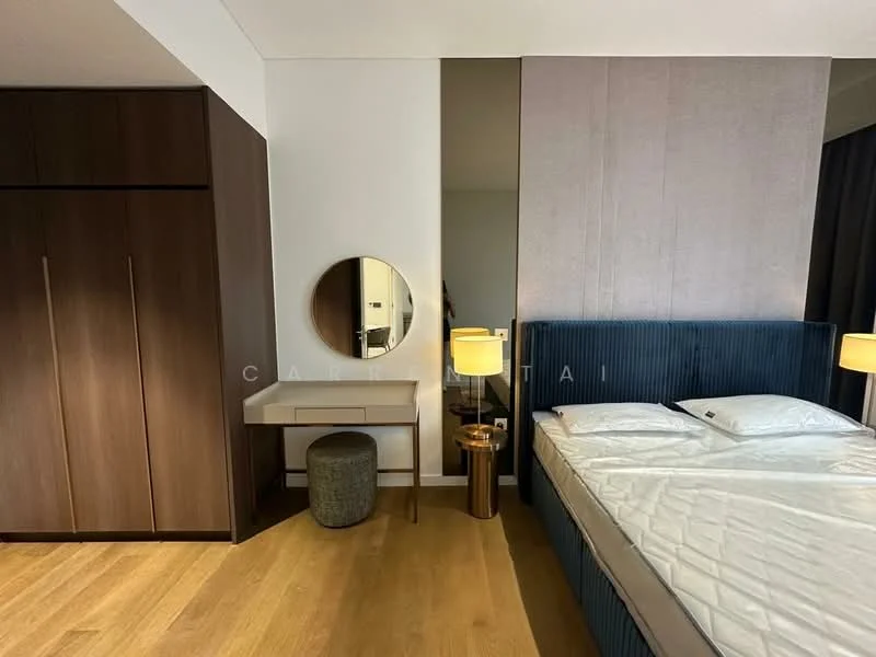 Bedroom features: king-size bed, upholstered headboard in navy blue, wooden flooring, built-in wardrobe with sliding doors, round mirror above a wooden vanity, table lamp on nightstand, small upholstered stool, decorative wall paneling, natural light from window, neutral wall color; style: modern.