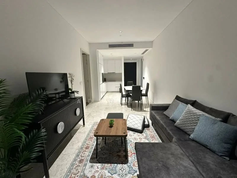 Living features: grey fabric sectional sofa, wood coffee table, area rug with geometric pattern, wall-mounted TV, black TV console with circular speakers, potted plant, recessed downlights, white painted walls, marble tile flooring; style: modern. Kitchen features: white cabinetry, black countertop, built-in oven, stainless-steel sink, chrome pull-down faucet, open-plan layout; style: modern. Dining features: 4-seater dining table, black dining chairs; style: modern.