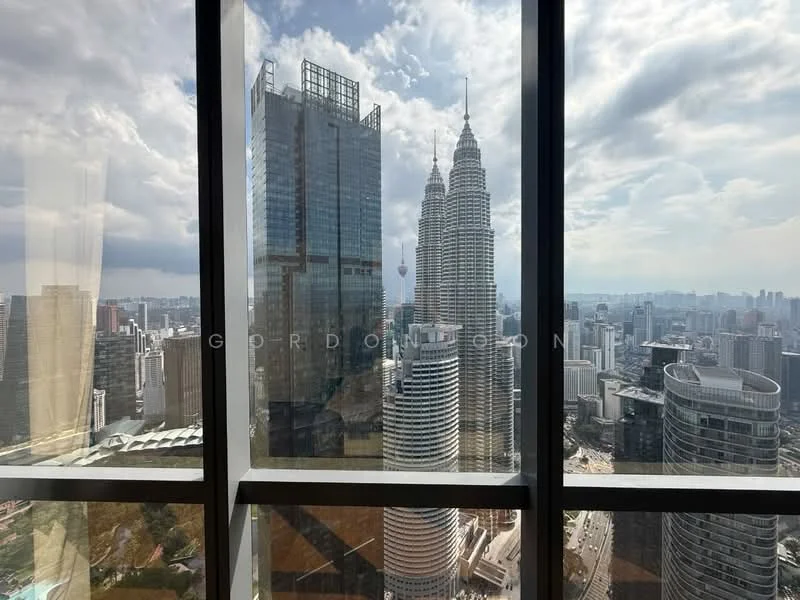 Exterior type: high-rise condominium; features: floor-to-ceiling windows, city skyline view, surrounded by skyscrapers, Petronas Twin Towers visible, modern glass facade, urban landscape, cloudy sky, high vantage point; style: modern.