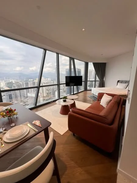 Living features: floor-to-ceiling windows, city view, brown leather sofa, coffee table, area rug, wall-mounted TV, dining table with chairs, decorative vase with flowers, wooden flooring, curtains, bed in background; style: modern; view: city.
