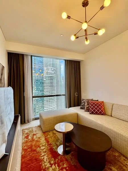 Living features: L-shape sectional sofa in beige, coffee table with round top, area rug with geometric pattern, floor-to-ceiling windows, curtains in dark grey, chandelier with multiple bulbs, wall-mounted TV, decorative cushions in red and white; style: modern; view: city.