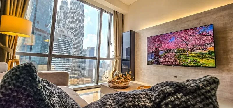 Living features: floor-to-ceiling windows, city skyline view, light grey walls, recessed LED downlights, wall-mounted TV, light-colored sofa, decorative throw pillows, coffee table, decorative vase with flowers, curtains, wooden flooring; style: modern; view: city.
