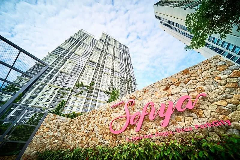 Exterior type: high-rise condominium; features: glass curtain wall, stone cladding at base, landscaped garden with greenery, signage with name 'Sofiya', surrounded by mature trees, modern architectural design; style: modern.