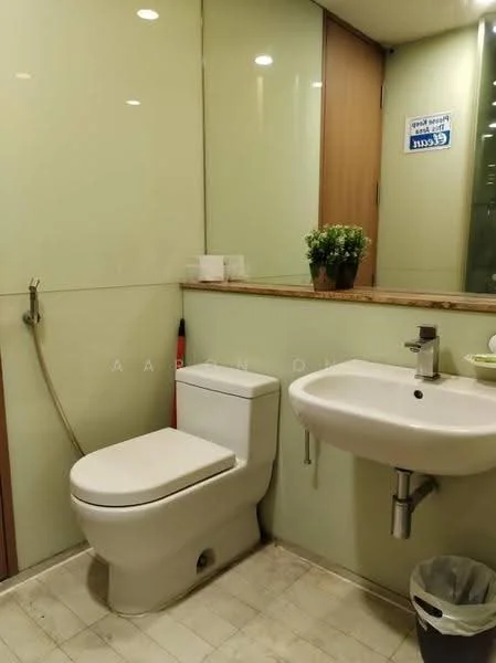 Bathroom features: one-piece toilet, wall-mounted sink, chrome basin mixer faucet, mirror above sink, granite countertop, glass wall, light-colored tile flooring, green potted plant, tissue box, waste bin; style: modern.