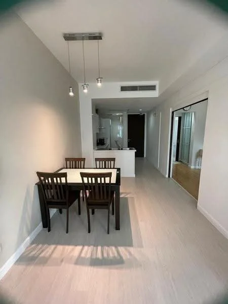 Dining features: 4-seater dining table, black wooden dining chairs, pendant lighting with three bulbs, light-colored laminate flooring, white painted walls, open layout to kitchen, sliding door to hallway, kitchen island visible in background; style: modern.