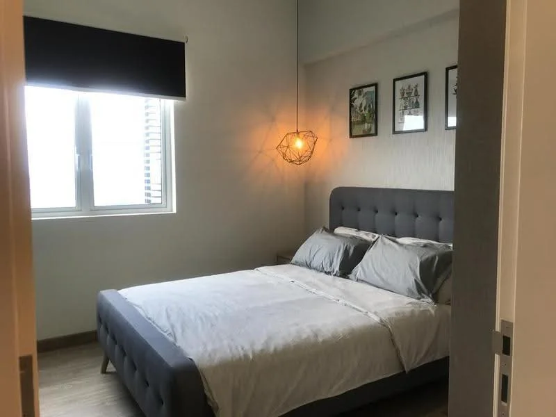 Bedroom features: queen-size bed with grey upholstered headboard, bedding in light grey, two bedside tables, pendant light fixture, framed artwork on walls, floor-to-ceiling window, black roller blinds, wooden flooring, light grey wall paint; style: modern.