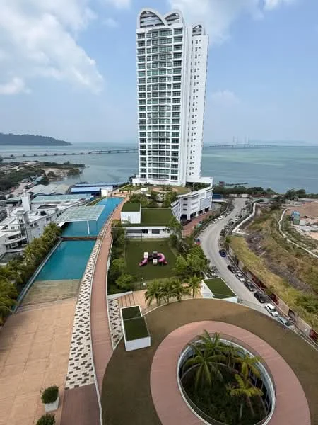 Exterior type: high-rise condominium; features: glass curtain wall facade, approximately 20-storey high-rise, infinity pool, landscape garden, manicured lawn, paved walkway, surrounded by mature greenery, sea view, parking area, children's playground; style: modern.
