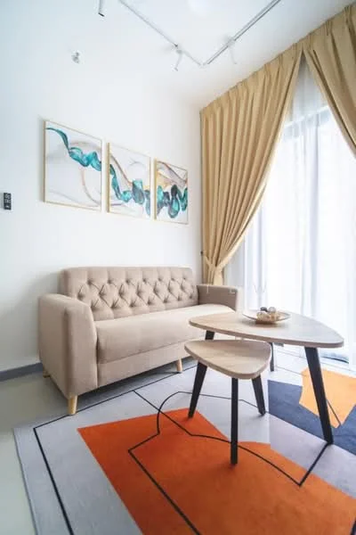 Living features: beige tufted fabric sofa, wooden coffee table, area rug with geometric pattern, framed artwork on walls, floor-to-ceiling windows, sheer curtains, recessed ceiling lights, light grey walls, wooden flooring; style: modern.