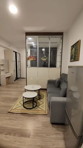Living features: grey fabric sofa, 2 coffee tables with white tops and black bases, wooden flooring, glass display cabinet, framed artwork on wall, curtains, refrigerator, area rug with geometric pattern, wall-mounted lighting; style: modern.