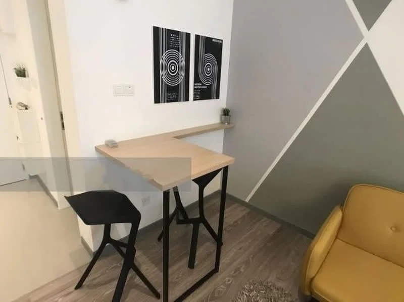 Room features: wooden bar table with light wood top, black metal legs on bar table, black bar stool, yellow accent chair, white walls, grey accent wall, decorative wall art with circular patterns, small potted plant on table, laminate flooring; style: modern.