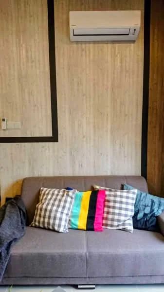 Living features: grey fabric sofa, plaid throw pillows in black and white, colorful striped pillow, blue throw blanket, wall-mounted split AC, textured wall with vertical lines, dark accent trim, light-colored flooring; style: modern.