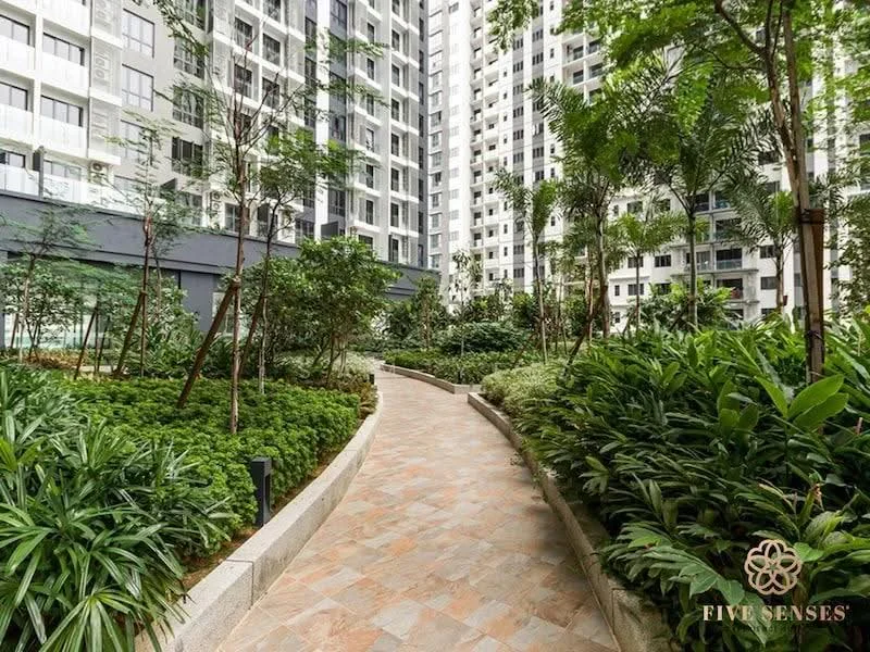 Exterior type: high-rise condominium; features: landscaped garden, paved walkway, mature trees, tropical landscaping, surrounding greenery, multiple high-rise buildings in background; style: modern.