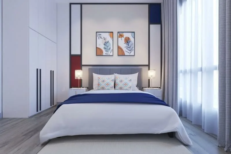 Bedroom features: king-size bed with white bedding and blue throw, upholstered headboard, two bedside tables with lamps, framed artwork on the wall, white walls with accent panels in red and blue, floor-to-ceiling windows with sheer curtains, wooden flooring, area rug; style: modern.