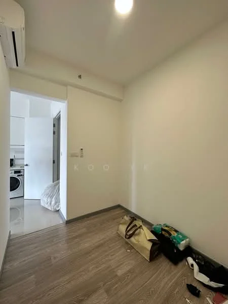Room features: white painted walls, laminate flooring, 1 wall-mounted split AC, ceiling light, doorway leading to another room, laundry area visible through doorway, no visible furniture, bags on the floor.
