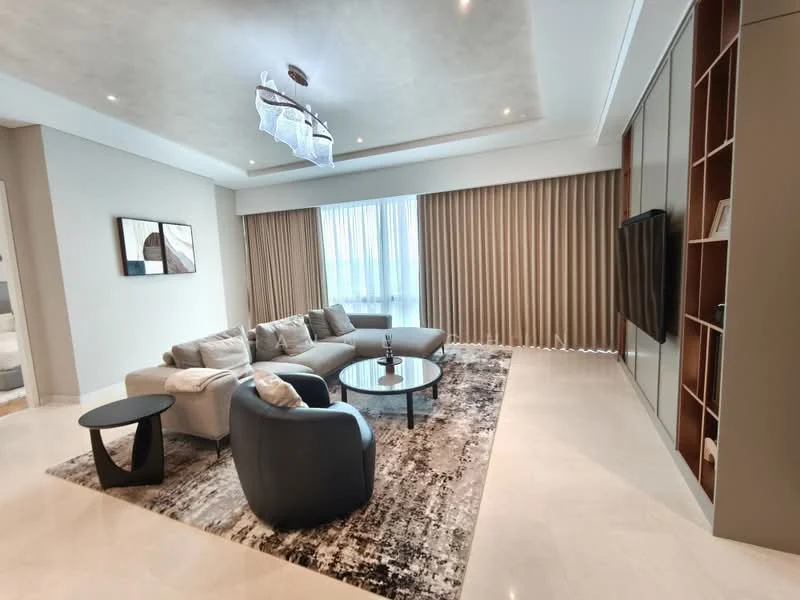 Living features: 3-seater fabric sofa in light grey, 2-seater accent chair in navy blue, round glass coffee table, area rug with abstract pattern, wall-mounted TV, built-in cabinetry with wood finish, floor-to-ceiling windows with sheer curtains, recessed downlights, chandelier with modern design, cream painted walls, marble flooring; style: modern.
