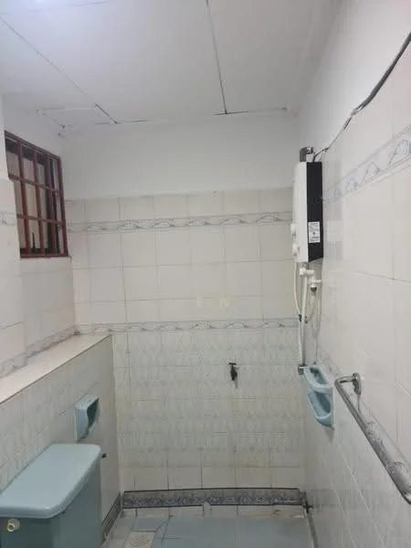 Bathroom features: white tiled walls, light blue patterned tiles, white toilet, wall-mounted water heater, sink with faucet, floor tiles, window with metal grille, shelf above sink.