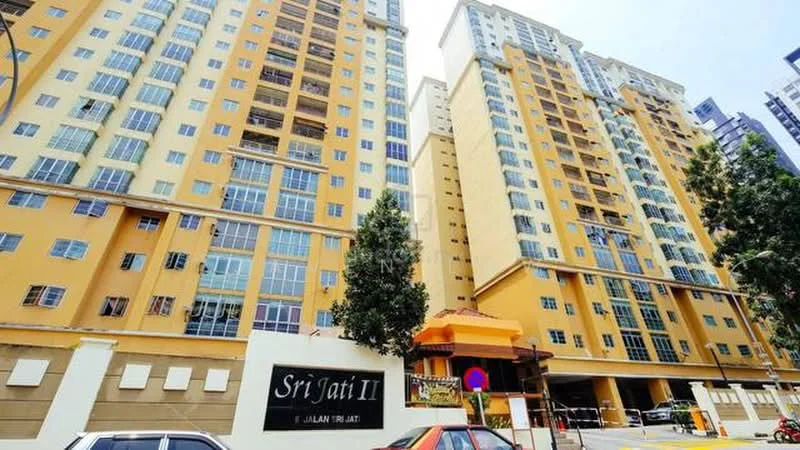 Exterior type: high-rise condominium; features: yellow painted facade, glass windows, multiple balconies, entrance with awning, surrounded by trees, parking area, security gate, signage at entrance; style: modern.