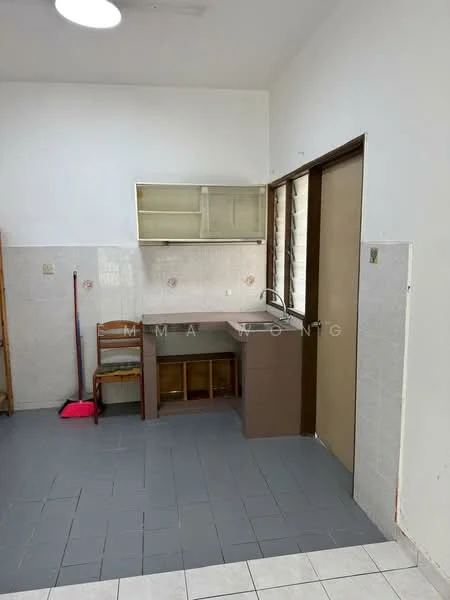 Kitchen features: grey tiled flooring, white painted walls, brown cabinetry, single-bowl stainless-steel sink, chrome pull-down faucet, wall-mounted kitchen shelves, window with horizontal slats, broom and dustpan visible.
