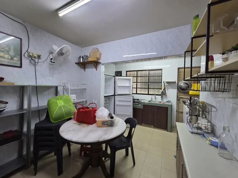 Kitchen features: white tiled walls, light beige tiled flooring, ceiling-mounted fluorescent lighting, round dining table, black plastic chairs, open shelving, stainless-steel sink, built-in cabinets with wood finish, refrigerator, kitchen countertop, kitchen utensils visible, fan mounted on wall.