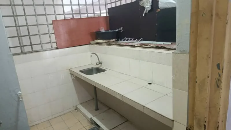 Kitchen features: single-bowl stainless-steel sink, chrome faucet, white tiled countertop, white tiled backsplash, light beige floor tiles, open shelving above sink, metal drying rack, window with grid pattern, exposed wall with paint peeling, wooden cabinet below countertop.